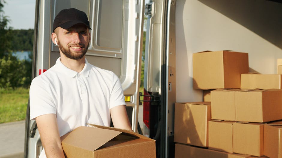 Two movers from Man with Van Surrey, dressed in navy uniforms, are engaged in a home relocation process, carefully lifting a large, dark green fabric-covered piece of furniture into the back of a whit